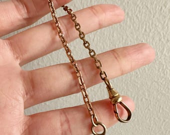 May include: A vintage gold-toned watch chain with a spring clasp and a small ring. The chain is composed of rectangular and oval links. The clasp and ring are attached to the chain.