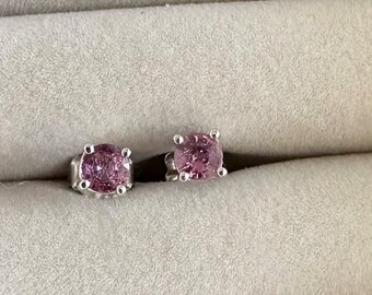 May include: A pair of stud earrings with a square-cut, light purple gemstone set in a silver metal. The earrings are displayed on a gray surface, showcasing their color and design. The gemstones appear to be approximately 0.25 inches in size.