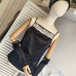 May include: A black satin top with a silver sequined trim around the neckline. The top is sleeveless and has a relaxed fit.