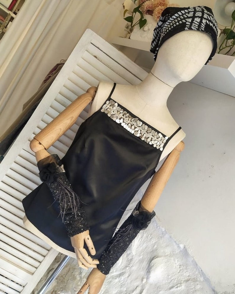 May include: A black satin top with a silver sequined trim around the neckline. The top is sleeveless and has a relaxed fit.