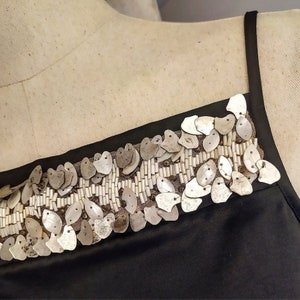 May include: A black sleeveless top with a decorative trim of silver and white sequins. The sequins are arranged in a pattern of overlapping ovals.