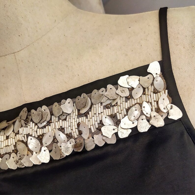 May include: A black sleeveless top with a decorative trim of silver and white sequins. The sequins are arranged in a pattern of overlapping ovals.