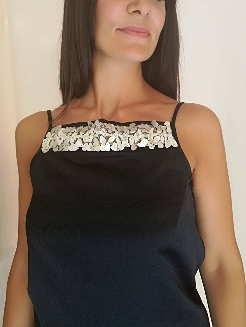 May include: A black sleeveless top with a silver sequined band across the neckline.