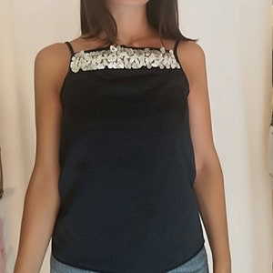 May include: A black sleeveless top with a silver sequined neckline. The top is made of a silky material and has a relaxed fit.