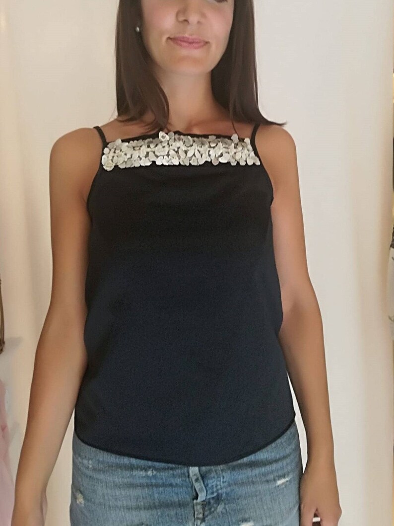 May include: A black sleeveless top with a silver sequined neckline. The top is made of a silky material and has a relaxed fit.