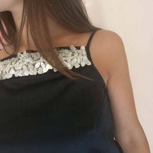 May include: A black sleeveless top with a silver sequined trim across the neckline.