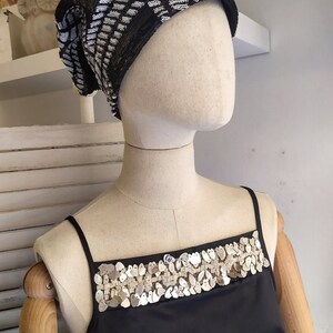 May include: A black sleeveless top with a silver sequined trim around the neckline. The top is on a white mannequin.