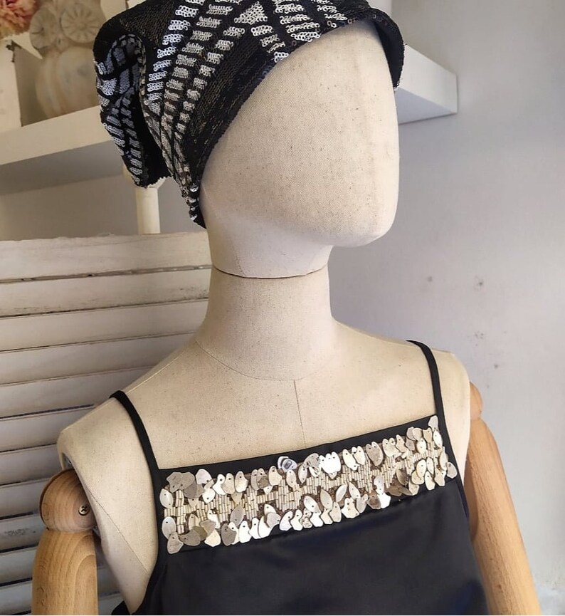 May include: A black sleeveless top with a silver sequined trim around the neckline. The top is on a white mannequin.