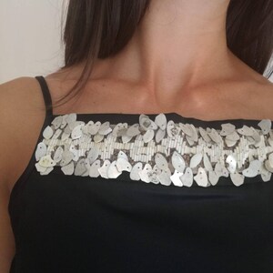 May include: A black sleeveless top with a silver sequined trim around the neckline.