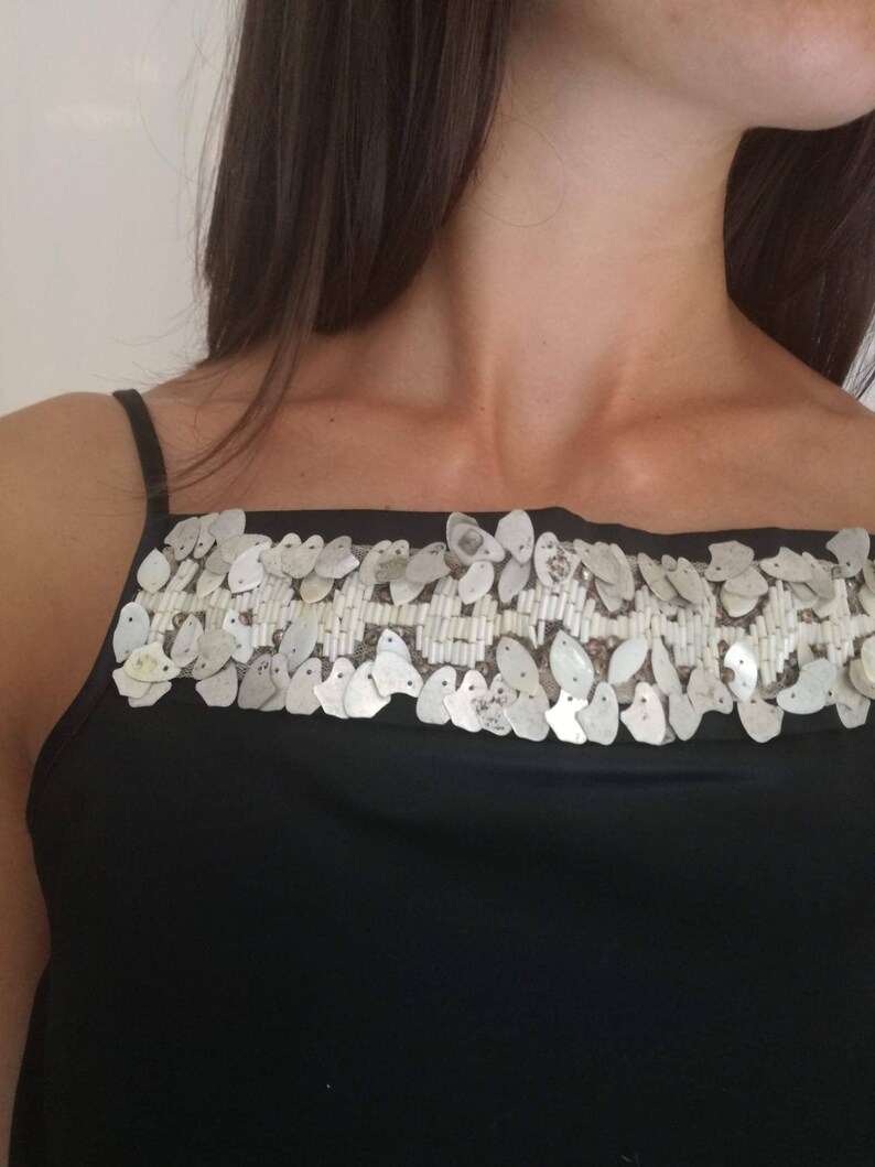 May include: A black sleeveless top with a silver sequined trim around the neckline.