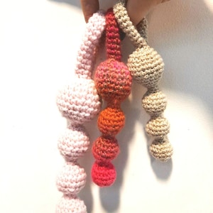 May include: Three crocheted strands of beads, each with a different color scheme. The strands are pink, orange and beige. The beads are all round and have a textured surface.