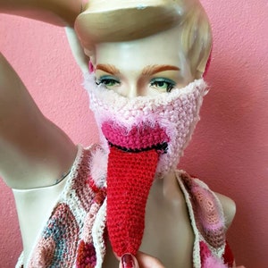 Könnte beinhalten: Eine rosa und weiße gehäkelte Gesichtsmaske mit einer roten gehäkelten Zunge, die herunterhängt. Die Maske wird von einer Mannequin mit blonden Haaren getragen. Der Text "House Of Daan" ist in der oberen rechten Ecke des Bildes sichtbar.