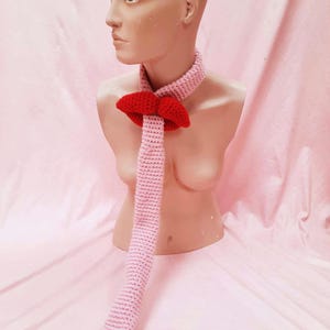 May include: A pink crocheted tie with a red bow. The tie is long and hangs down to the floor.