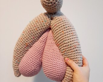 May include: A crocheted plush toy in the shape of a human figure with a round head and two pink teardrop-shaped appendages.