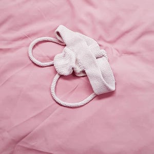 May include: A white crocheted bag with a single handle. The bag is lying on a pink surface.
