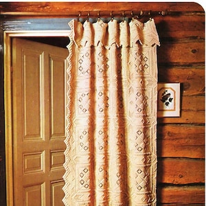 May include: A crocheted curtain with a geometric pattern hangs in a rustic wooden cabin. The curtain is cream-colored and has a scalloped edge. A vase of flowers sits in front of the curtain.