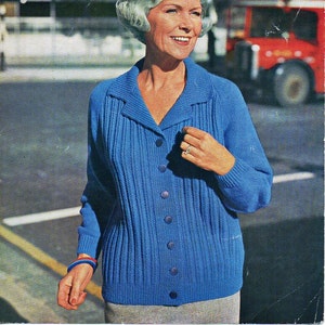 May include: A blue knitted cardigan with a collar and button closure. The cardigan is being worn by a woman with white hair. The text on the image reads "Wendy Double Knitting 38/42" Bust 9p 680".