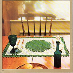 Puede incluir: Un mantel individual de ganchillo verde con un encaje redondo en el centro. El mantel individual está sobre una mesa de madera con un vaso de agua, una botella de vino y dos tenedores.