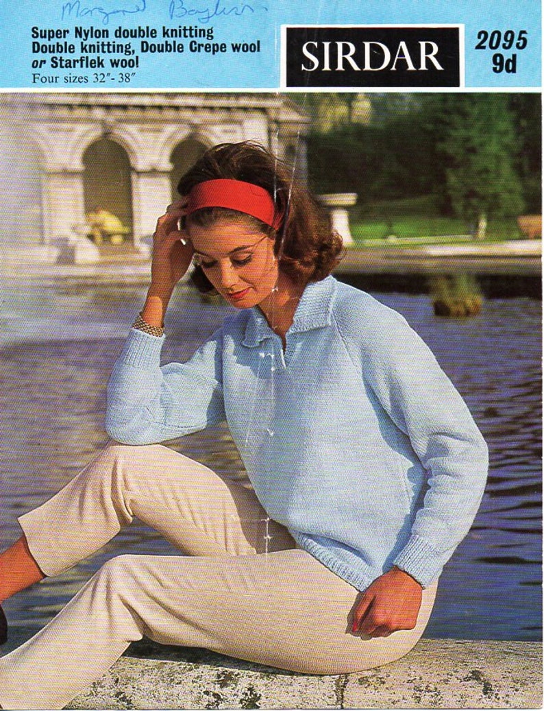 May include: A light blue knitted sweater with a collared neckline. The sweater is worn by a person sitting on a stone ledge by a pond. The text "SIRDAR 2095 9d" is visible in the upper right corner of the image.