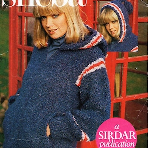 Puede incluir: Un suéter azul con capucha con rayas blancas y rojas. El suéter está siendo modelado por una mujer con cabello rubio. La imagen también incluye una cabina telefónica roja y el texto "a Sirdar publication" y "As featured in Woman's Weekly".