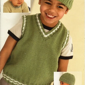 May include: A green knitted vest with white trim, worn by a young boy wearing a green knitted hat. The vest has a V-neck and a ribbed texture. The hat has a cable knit pattern. The boy is smiling. Design G.