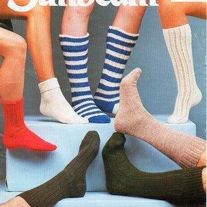 Peut inclure: Publicité présentant diverses chaussettes tricotées de différentes couleurs et motifs. Les chaussettes comprennent des modèles unis rouges, blancs, à rayures bleues et côtelés. Le mot "Sunbeam" est affiché en haut, avec du texte indiquant que les chaussettes sont 3 plis, 4 plis et DK.