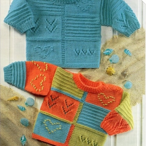 Könnte beinhalten: Zwei gestrickte Pullover mit bunten Patchwork-Designs und Stickereien. Die Pullover liegen auf einer sandigen Oberfläche mit Muscheln.