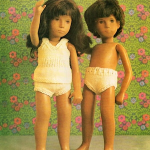 Puede incluir: Dos muñecas con ropa interior de punto blanco. La muñeca de la izquierda tiene el pelo largo y castaño y lleva un top sin mangas. La muñeca de la derecha tiene el pelo corto y castaño.