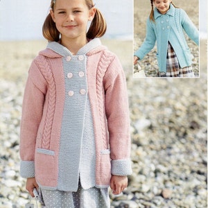 May include: A pink and grey knitted cardigan with a hood and buttons. The cardigan has a cable knit pattern and pockets on the sides. The model is wearing a white polka dot dress underneath.