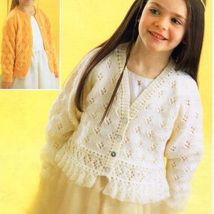 Könnte beinhalten: Zwei Mädchen tragen weiße und gelbe Strickjacken mit einem Spitzenmuster. Die Jacke rechts hat einen Rüschen-Saum.