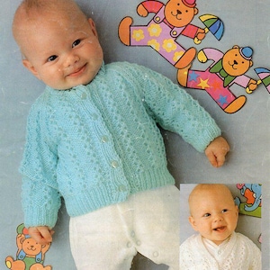 Peut inclure: Un bébé portant un cardigan en tricot bleu clair avec une fermeture à boutons. Le cardigan a un motif en tricot torsadé. Le bébé porte un pantalon blanc et est assis sur une surface bleu clair. Il y a des ours en peluche colorés en arrière-plan.