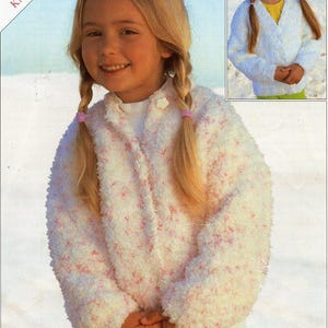 Op de afbeelding: Een wit en roze gebreid vest met knoopsluiting. Het vest wordt gedragen door een jong meisje met blond haar.