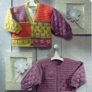 Może przedstawiać: Dwa dzianinowe kardigany z zapięciem na guziki i haftowanymi kwiatowymi detalami. Kardigan po lewej stronie jest wielokolorowy z patchworkowym wzorem. Kardigan po prawej stronie jest jednokolorowy, fioletowy.