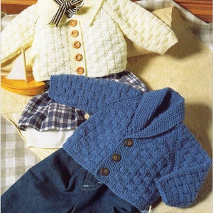 May include: Two knitted baby cardigans, one white with a black and white bow and the other blue with a collar. Both cardigans have button closures.