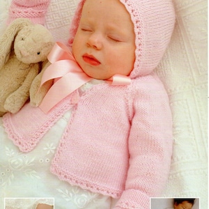 May include: A pink knitted baby cardigan with matching hat and booties. The cardigan has a button closure and a scalloped edge. The hat has a scalloped edge and a tie at the back. The booties have a scalloped edge and a pointed toe.