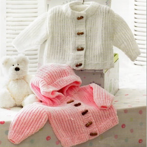May include: Two knitted baby sweaters, one white and one pink. The pink sweater has a hood and both sweaters have wooden buttons.