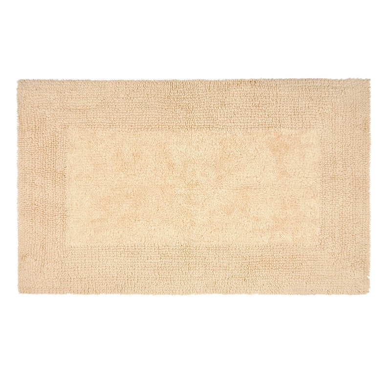 May include: A beige bath mat with a slightly darker border. The mat is made of a soft, absorbent material.