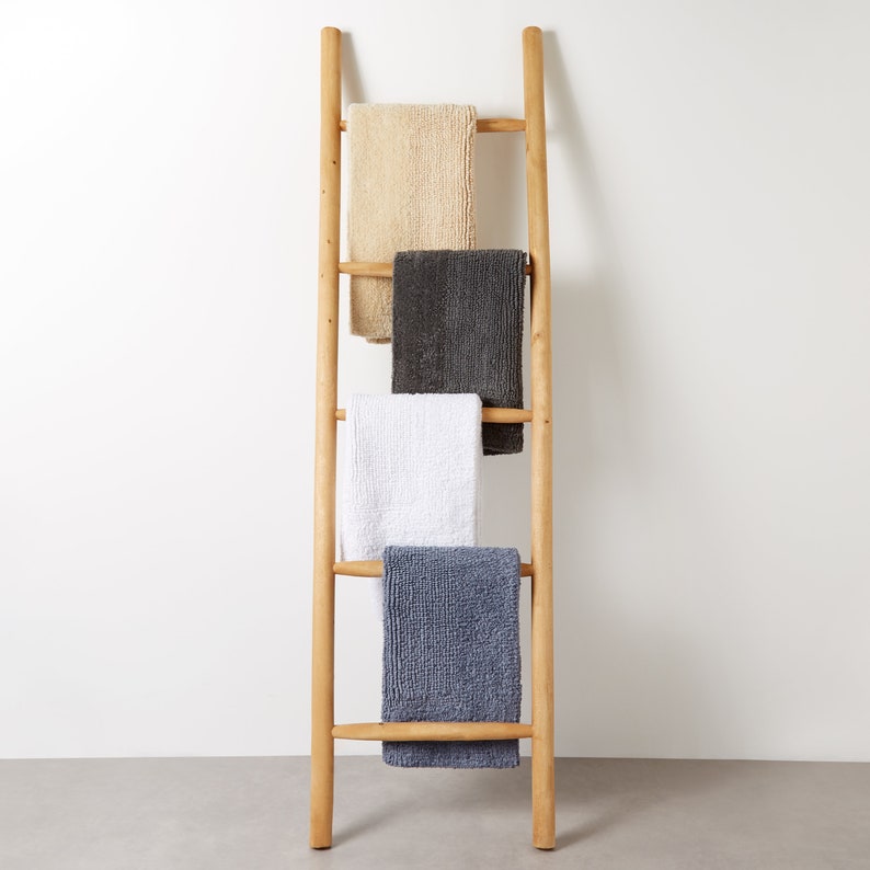 May include: A wooden ladder with four towels hanging on it. The towels are beige, gray, white, and blue.