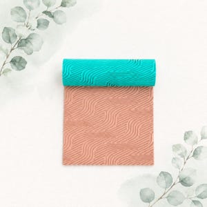 May include: A rectangular clay texture sheet featuring a raised, wavy, topographical line pattern. The top section is a vibrant turquoise color, while the bottom section is a muted terracotta orange, both displaying the same continuous relief design.