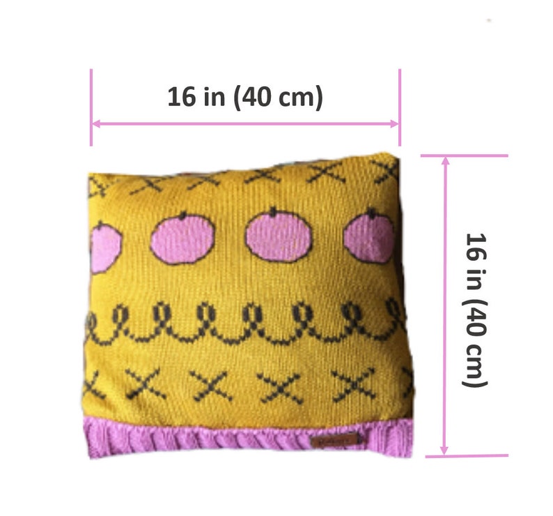 May include: A square, knitted pillow, 16 inches (40 cm) on each side, with a mustard yellow background. The pillow features pink fruit designs, black cross and squiggle patterns, and a pink border. A small label is visible.