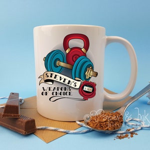 May include: White ceramic mug featuring a colourful illustration of a dumbbell, kettlebell, and a stopwatch. The text "Steven's Weapons of Choice" is printed on the mug.