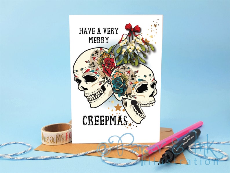 May include: A white greeting card with a festive message that reads "Have a Very Merry Creepmas". The card features two colorful sugar skulls with floral designs and a sprig of mistletoe with a red bow.
