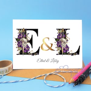 May include: A white card with black and gold lettering. The letters E and L are decorated with purple roses, skulls, and daggers. The text reads "E & L Elliot & Libby".