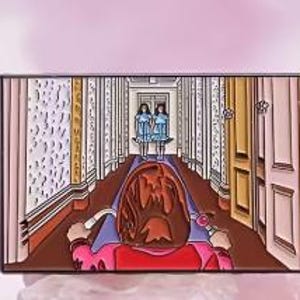 May include: A rectangular enamel pin featuring a scene from a horror film. The pin depicts a hallway with two girls in blue dresses, a person in a wheelchair, and a brown frame. The pin has a pink, brown, and blue color scheme.