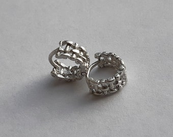 May include: A pair of silver hoop earrings with a woven design.