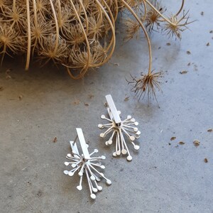 May include: A pair of silver earrings with a delicate, starburst design. The earrings are made of metal and have a polished finish.