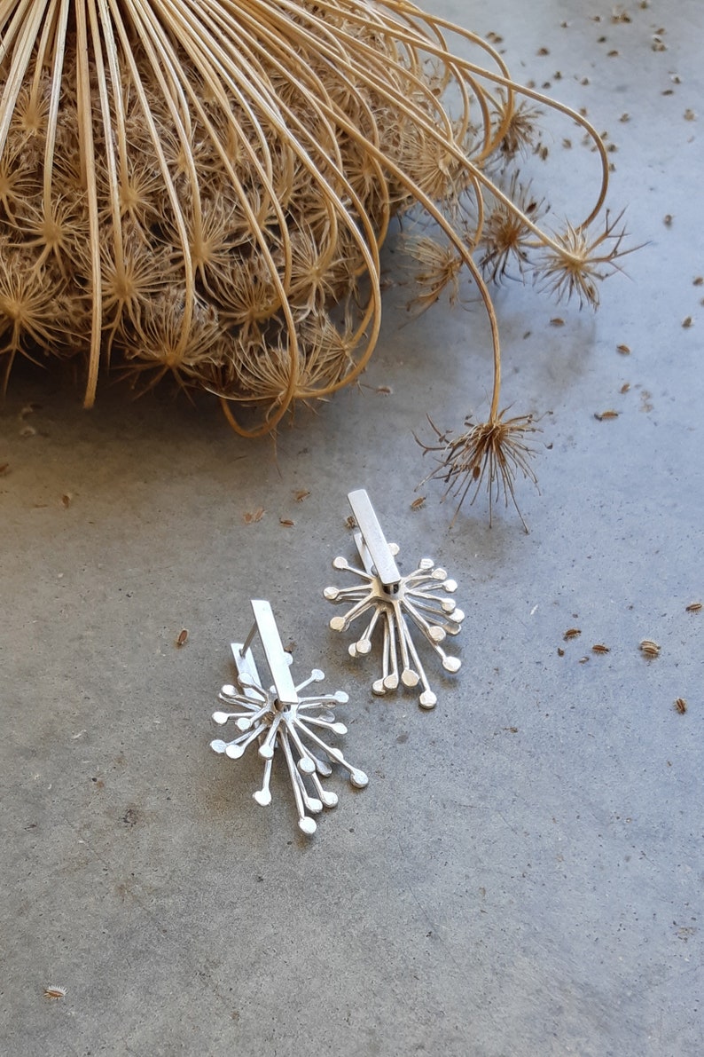 May include: A pair of silver earrings with a delicate, starburst design. The earrings are made of metal and have a polished finish.