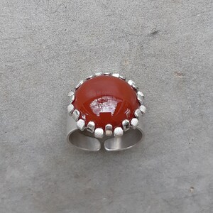 May include: A silver ring with a red carnelian gemstone set in a silver bezel. The ring has a textured silver band.