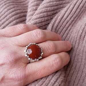 May include: A silver ring with a large, round, reddish-brown carnelian gemstone set in a textured silver bezel.