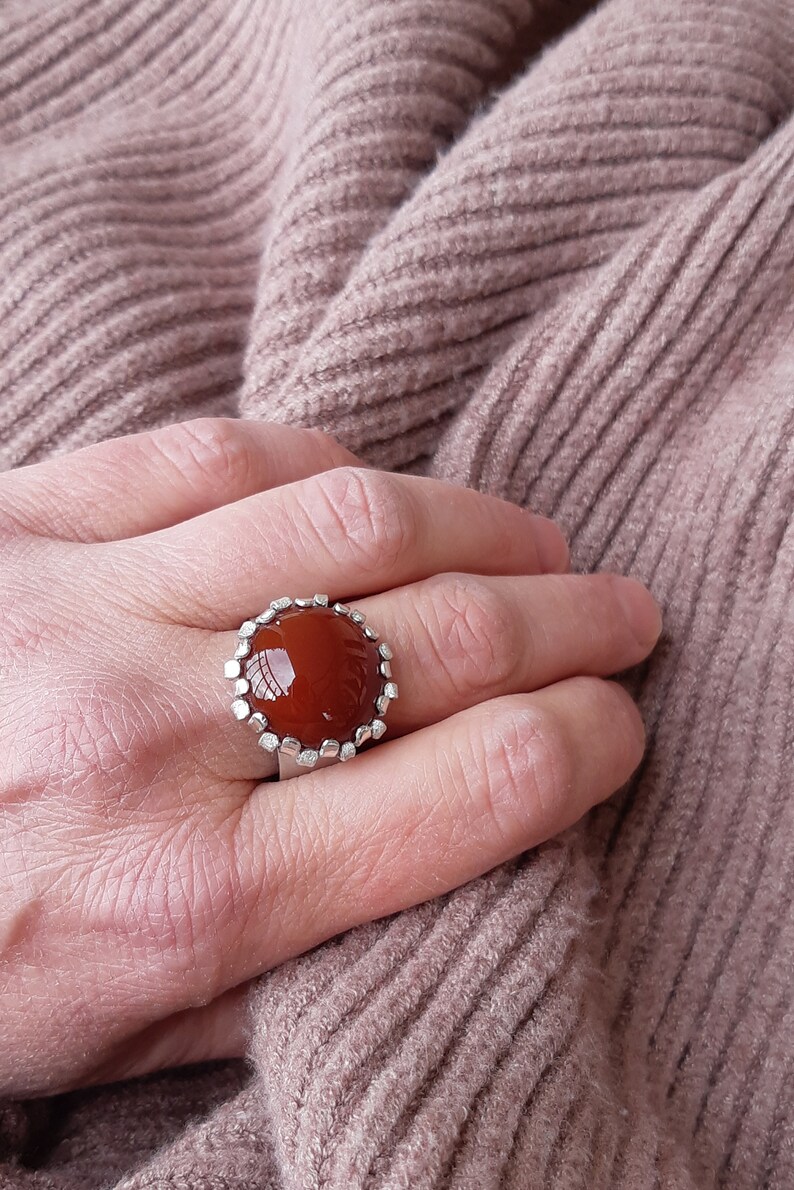 May include: A silver ring with a large, round, reddish-brown carnelian gemstone set in a textured silver bezel.